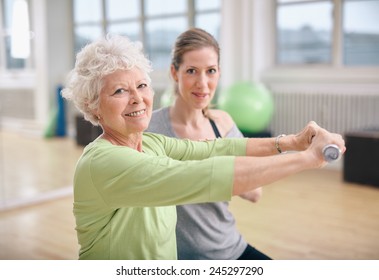 Senior woman exercising with fitness trainer at gym. Active senior woman lifting dumbbells with help from personal trainer.