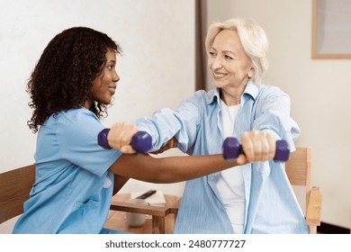 Senior Woman Exercising With Nurse Using Dumbbells, Smiling And Encouraging In Bright Room. Healthy Lifestyle, Rehabilitation, Physical Therapy Support. - Powered by Shutterstock