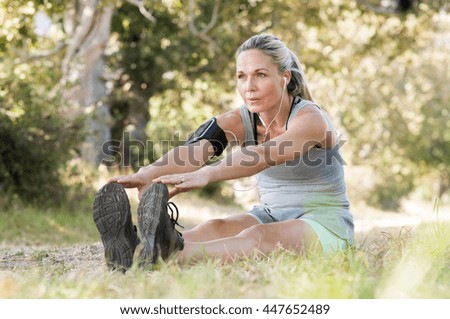 Senior woman exercising in park while listening to music. Senior woman doing her stretches outdoor. Athletic mature woman stretching after a good workout session.