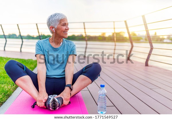 Senior woman exercising in park\
while listening to music. Senior woman doing her stretches outdoor.\
Athletic mature woman stretching after a good workout\
session.
