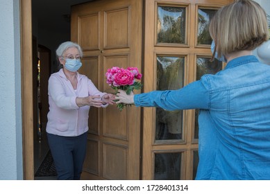 Senior Woman With Face Mask Gets Flowers At The House Door From Neighbor Woman