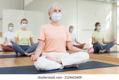 Senior woman in face mask sitting on mat in lotus pose during group yoga training with her family. - Powered by Shutterstock