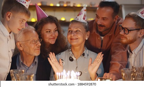 Senior woman with family and friends celebrating a birthday indoors. Happy aged female with cake surrounded by family having home party - Powered by Shutterstock