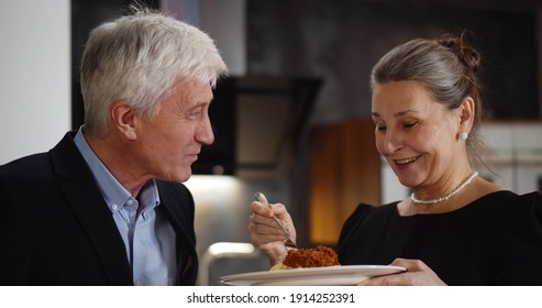 Senior Woman Feeding Husband With Delicious Pasta Having Dinner At Home. Close Up Portrait Of Elegant Aged Husband And Wife Having Meal Together In Kitchen