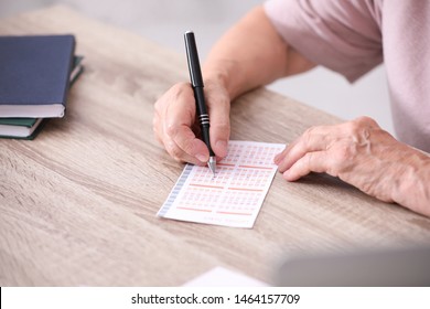 Senior Woman Filling Out Lottery Ticket At Table, Closeup