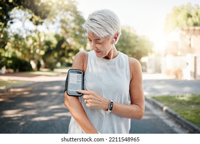 Senior Woman, Fitness And Phone Armband Listening To Music For Morning Run In An Urban Street Outdoors. Active Elderly Female Runner Checking Smartphone To Monitor Training Exercise Or Navigation