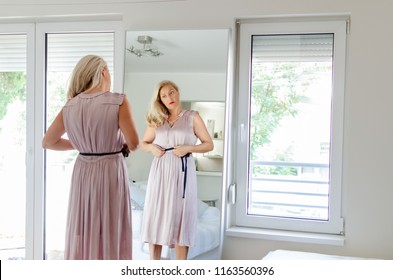 Senior Woman In Front Of Mirror Getting Ready, Wearing A Pink Dress.