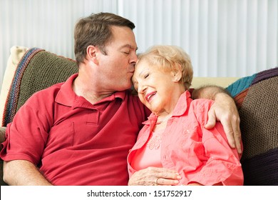 Senior woman gets a kiss from her loving adult son who has come to visit her in the nursing home.  
