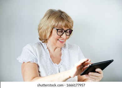 Senior Woman With Glasses Smiling Looking At A Computer Tablet On A White Background