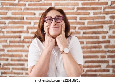 Senior woman with glasses standing over bricks wall smiling with open mouth, fingers pointing and forcing cheerful smile  - Shutterstock ID 2226158915