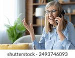 Senior woman with glasses talking on phone indoors looking upset or frustrated. Elderly lady having difficult conversation expressing emotions.