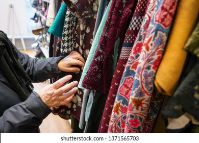 Senior Woman Going Through Clothes In Second Hand Thrift Charity Shop, Detail On Her Moving Hands.