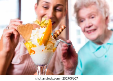 Senior Woman And Granddaughter Having Fun Eating Ice Cream Sundae In Cafe