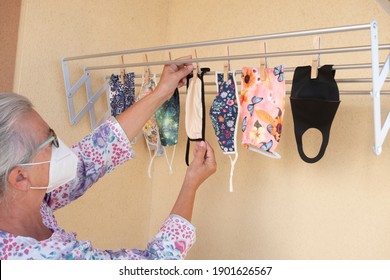 A Senior Woman With Gray Hair Hanging The Washed Family Protective Masks On The Clothesline To Dry - Homemade Masks With Fabric Useful Against Infection Of Virus Such As Covid-19 -large Family Of Seve