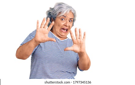 Senior woman with gray hair wearing casual striped clothes afraid and terrified with fear expression stop gesture with hands, shouting in shock. panic concept. 