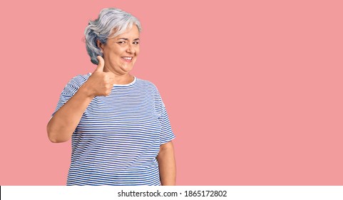 Senior woman with gray hair wearing casual striped clothes doing happy thumbs up gesture with hand. approving expression looking at the camera showing success. 