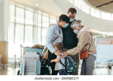 Senior woman greeting and welcoming family arriving at airport after pandemic lockdown. Couple and their child welcomed by their mother at airport. All wearing face masks.