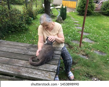 
Senior woman and grey cat in summer garden. 
