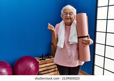 Senior woman with grey hair holding yoga mat screaming proud, celebrating victory and success very excited with raised arm 