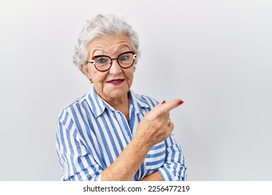 Senior woman with grey hair standing over white background with a big smile on face, pointing with hand and finger to the side looking at the camera.  - Powered by Shutterstock