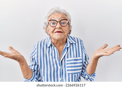 Senior woman with grey hair standing over white background clueless and confused expression with arms and hands raised. doubt concept.  - Powered by Shutterstock