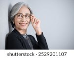 Senior woman with grey hair wearing a suit. President-like image. Wearing glasses and smiling.