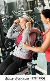 Senior Woman At Gym Exercise With Personal Trainer On Machine