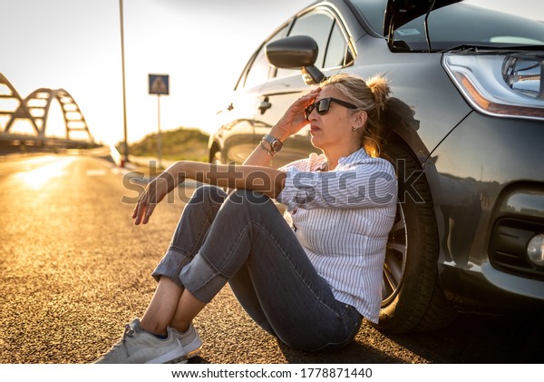Senior woman had car trouble in\
the middle of the street, sitting next to car and waiting for\
help