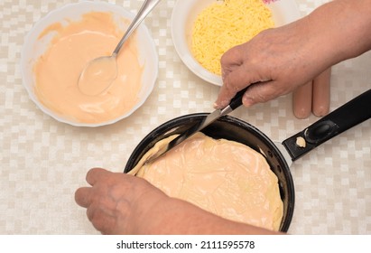 Senior Woman Hands Cut Off Excess Dough For Homemade Pizza On Black Pan With A Knife. Other Ingredients Are On The Table. Top View With Selective Focus. Process Of Cooking Pizza, Step 5