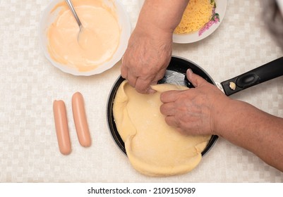 Senior Woman Hands Knead The Raw Dough On Black Pan With Oil For Homemade Pizza. Other Ingredients Are On The Table. Top View With Selective Focus. Process Of Cooking Pizza, Step 2