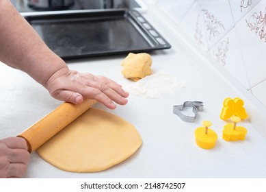 Senior woman hands rolling out the dough for cookies with a rolling pin on a white kitchen. Selective focus. Happy Easter concept. Process of making cookies. Cooking at home concept. 