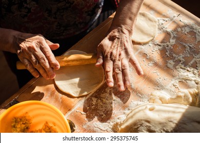 Senior woman hands rolling out dough in flour with rolling pin in her home kitchen