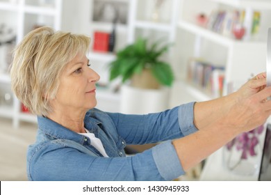 Senior Woman Hanging A Picture On The Wall