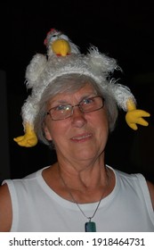 A Senior Woman Having Fun Wears A Silly Plush Chicken Hat On Her Head 