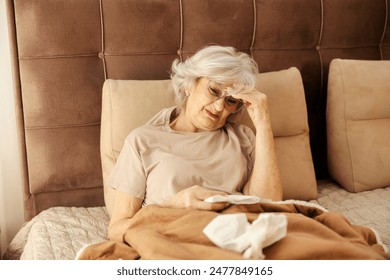 Senior woman having headache and flu symptoms and lying down in a bed surrounded by handkerchiefs. - Powered by Shutterstock