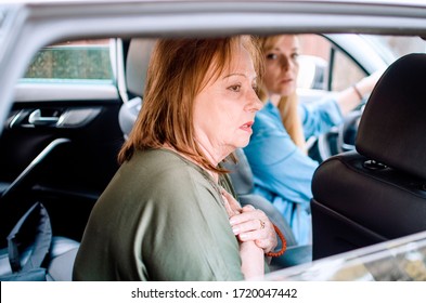 Senior Woman Having Heart Attack And Hard Breathing In A Car While Her Daughter Driving.Sick Old Breathless Lady Sitting On The Back Seat In A Car Holding Chest.Unwell Grandmother On Way To Hospital