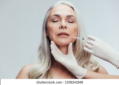 Senior woman having skin injections against grey background. Female getting anti aging shots on her face by beautician. - Powered by Shutterstock