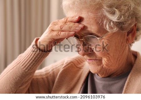 Senior woman with headache at home, closeup. Symptom of age-related memory impairment