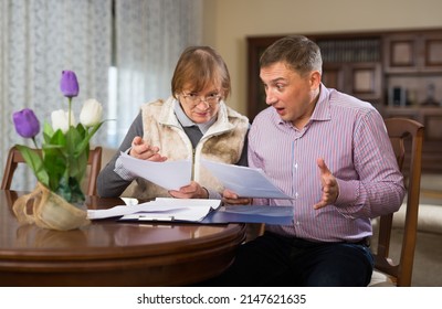 Senior Woman With Her Adult Son Filling Out Documents At Home