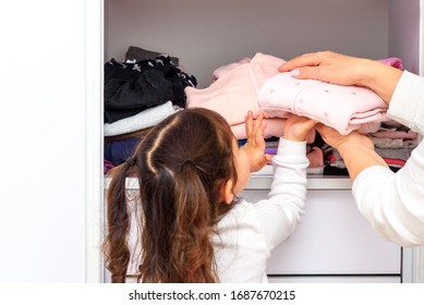 Senior woman with her grandchild storing clothes in wardrobe. Granddaughter and grandmother folding clean clothes. Close up of child and hands. - Powered by Shutterstock