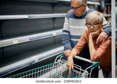 Senior Woman And Her Husband Feeling Concerned About Empty Shelves And Shortage Of Food In Supermarket.