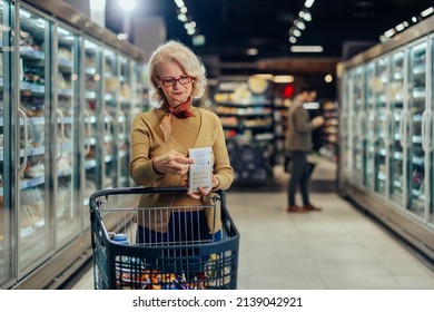 Senior woman in her shopping in a grocery store, standing beside shopping cart. She is reading the ingredient label on product. - Powered by Shutterstock