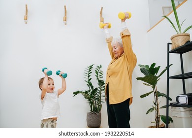 Senior Woman And Her Young Grandson Together Do Exercises By Lifting Dumbbells Up. High Quality Photo