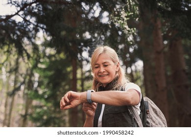 Senior woman hiker outdoors walking in forest in nature, using smartwatch. - Powered by Shutterstock