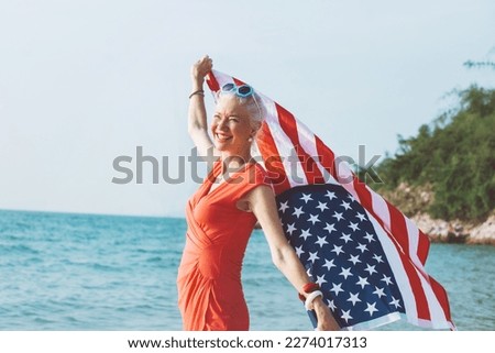 Senior woman holding american flag together on beach