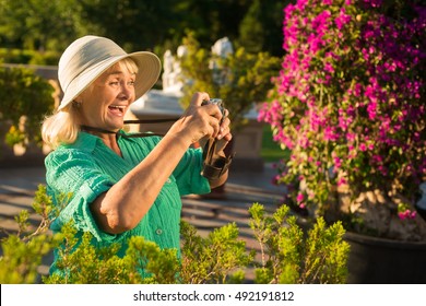 Senior Woman Holding Camera. Lady In Hat Is Laughing. Find Yourself A New Hobby. Amazing Life Around Us.