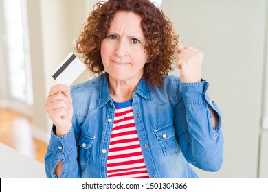 Senior woman holding credit card as payment annoyed and frustrated shouting with anger, crazy and yelling with raised hand, anger concept