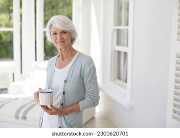 Senior woman holding cup of coffee in sun room - Powered by Shutterstock