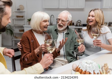 Senior Woman Holding Glass Of Wine And Laughing During Family Dinner