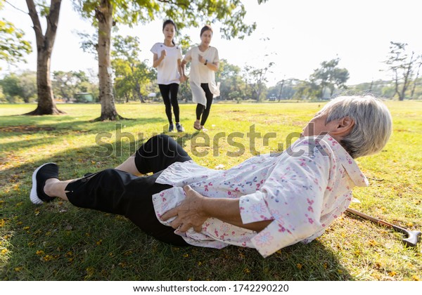 Senior woman is holding her hip,severe pain\
in her muscle,broken bone,injury to the waist,old elderly lying on\
the ground,she fell down while strolling,daughter,granddaughter ran\
to help grandmother